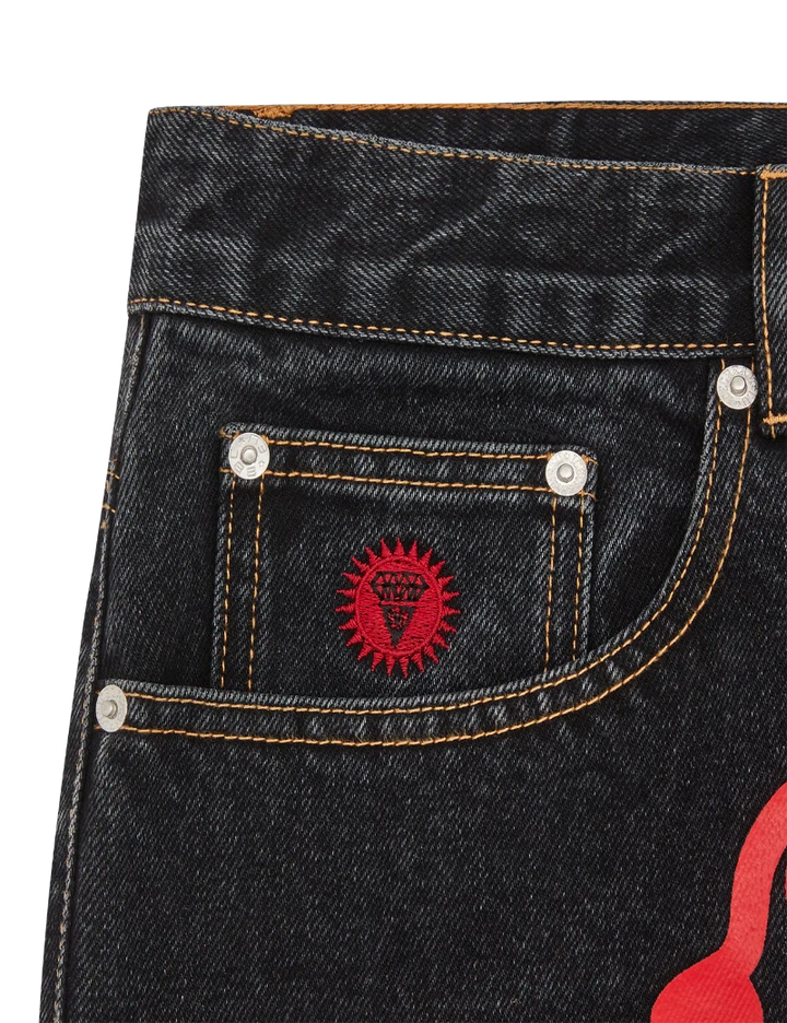 Close-up of a dark denim pocket with a red logo and stitching details.